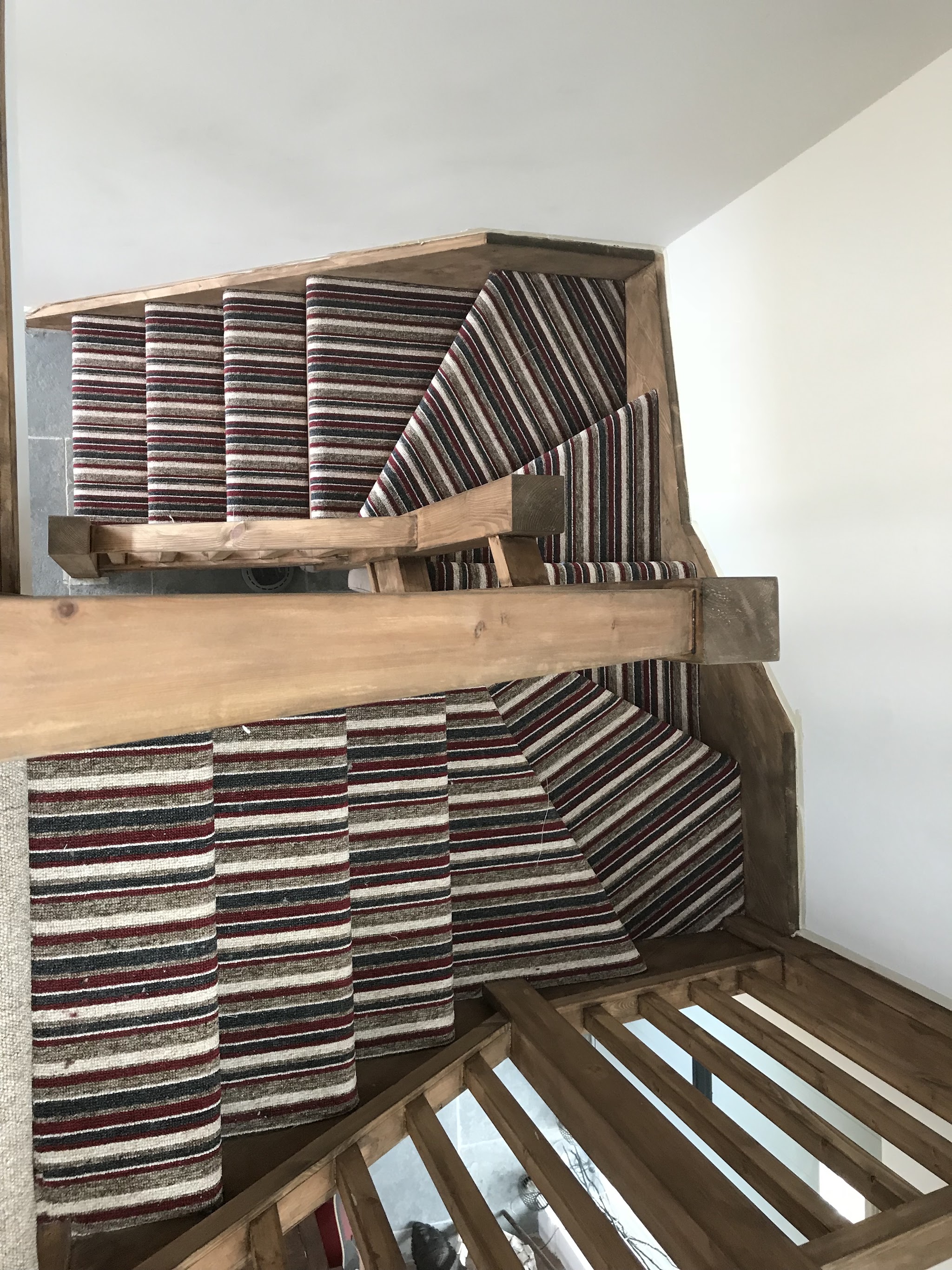 Striped stair carpet fitted on a winding staircase with an oak beam