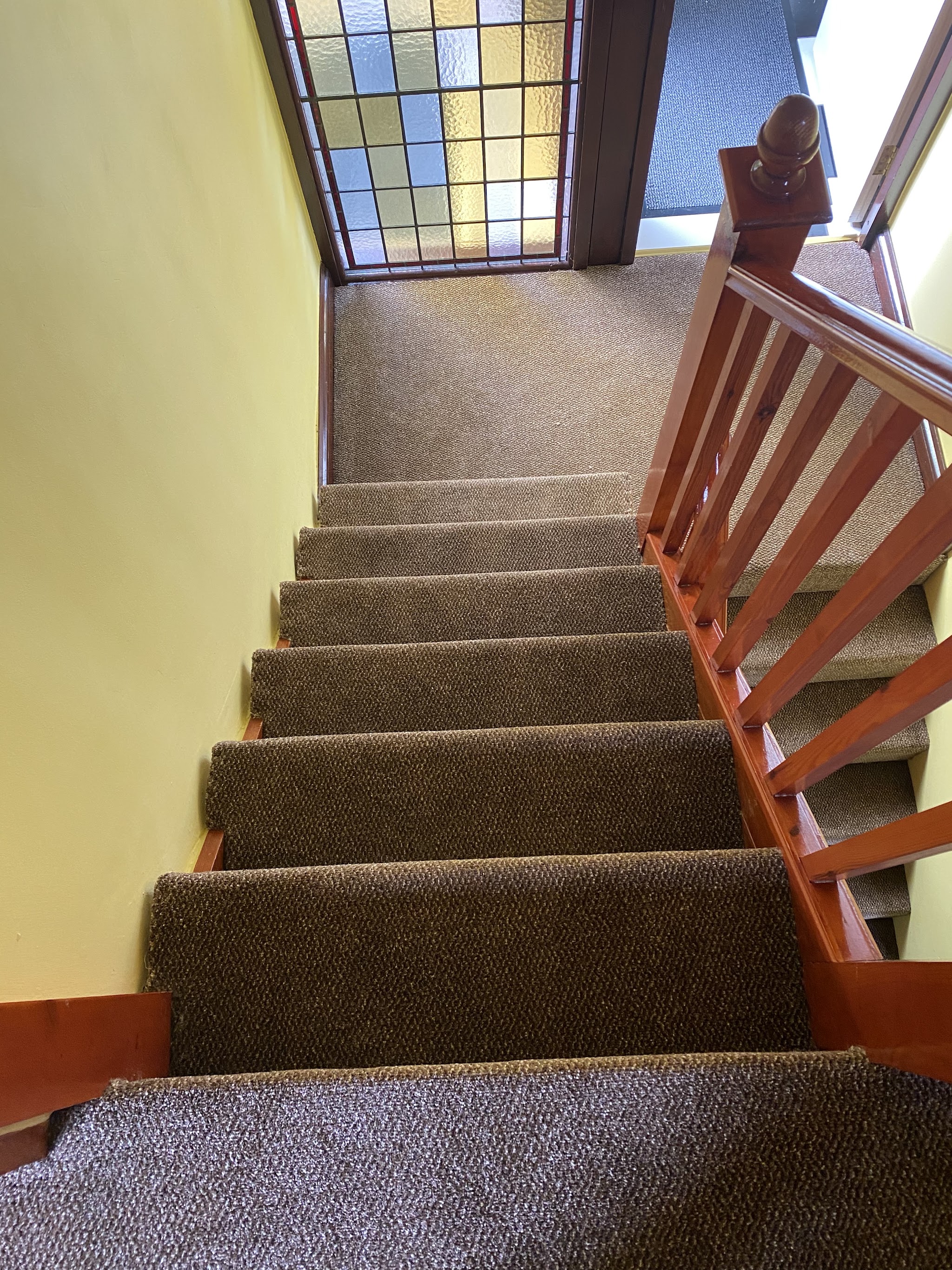 Brown carpet fitted on stairs below a stained glass window